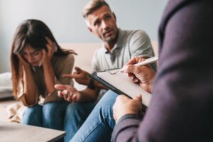 Photo of upset irritated couple man and woman having conversation with psychologist on therapy session in room