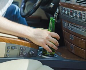 a person holding a beer bottle while driving a car